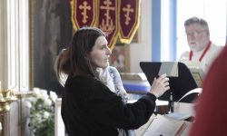 Matushka Beth directing choir while holding a small child. Richard Dauenhauer in the background